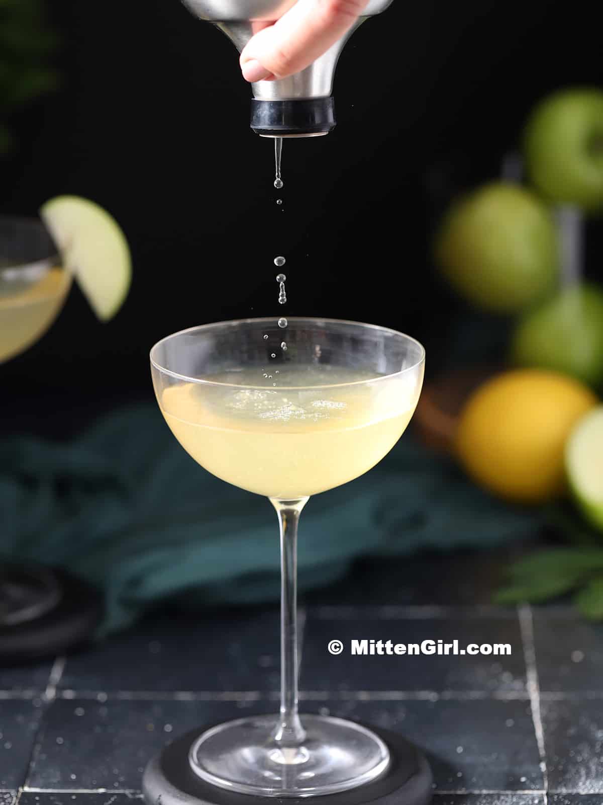 Pouring an apple martini into a coupe glass. 