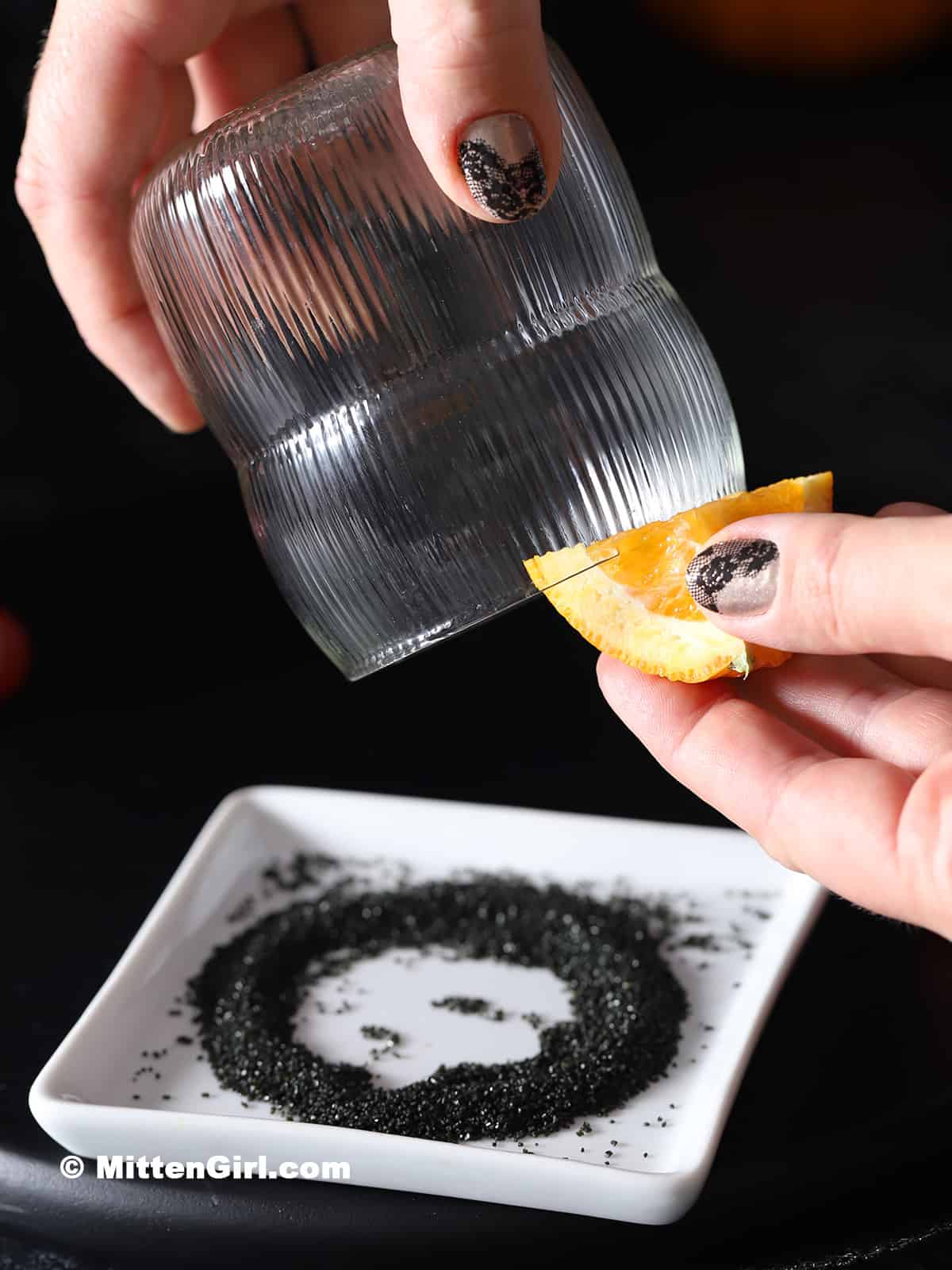 A hand holding an orange slice on the rim of a glass.