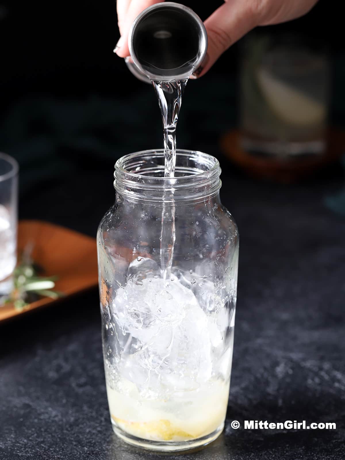 Gin being poured into a cocktail shaker filled with ice.