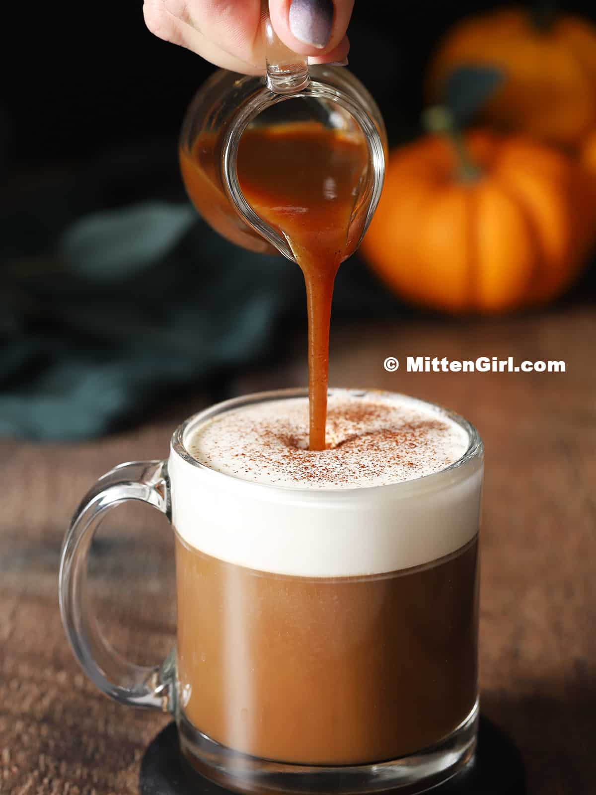 Pumpkin spice syrup being poured into a mug of coffee and cream. 