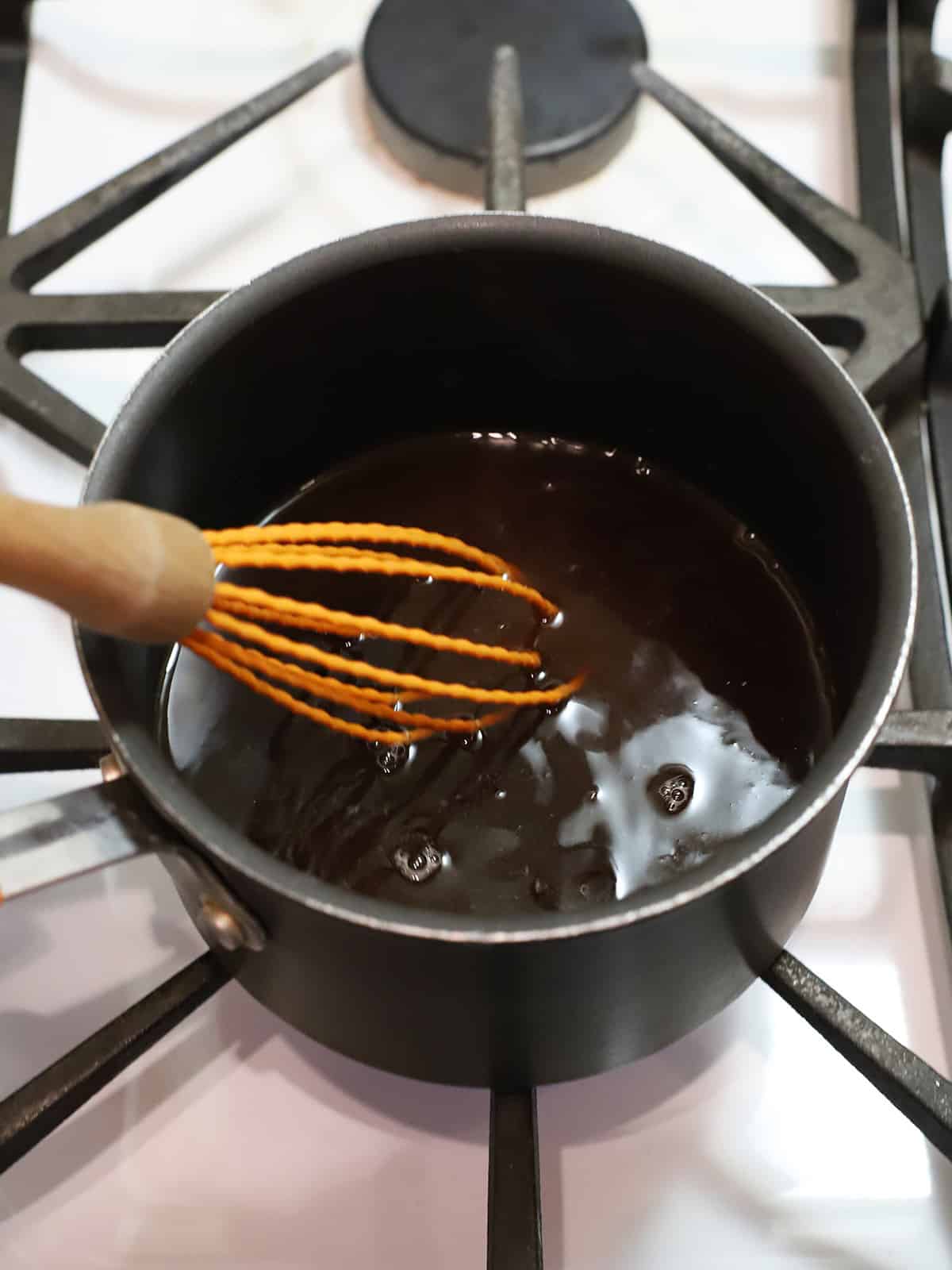 A pot with brown sugar and water being whisked together.