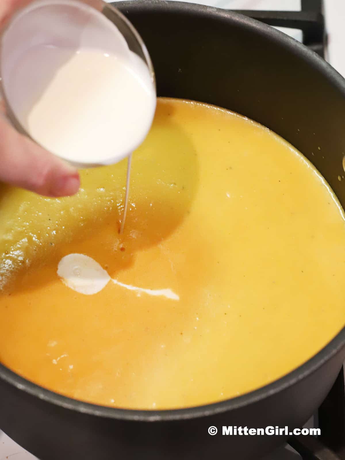 Heavy cream being added to a pot of soup.