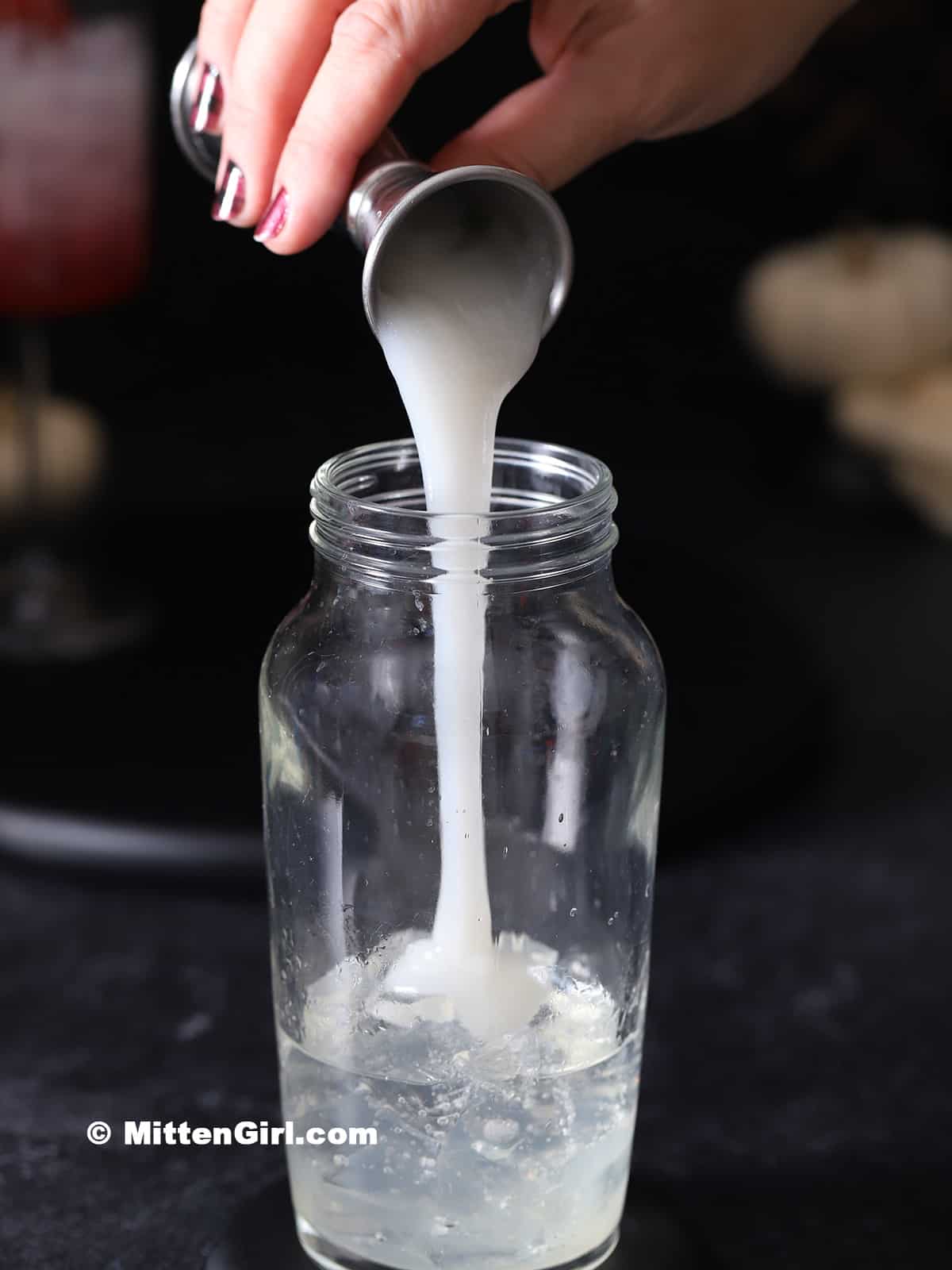 Cream of coconut being poured into a cocktail shaker. 