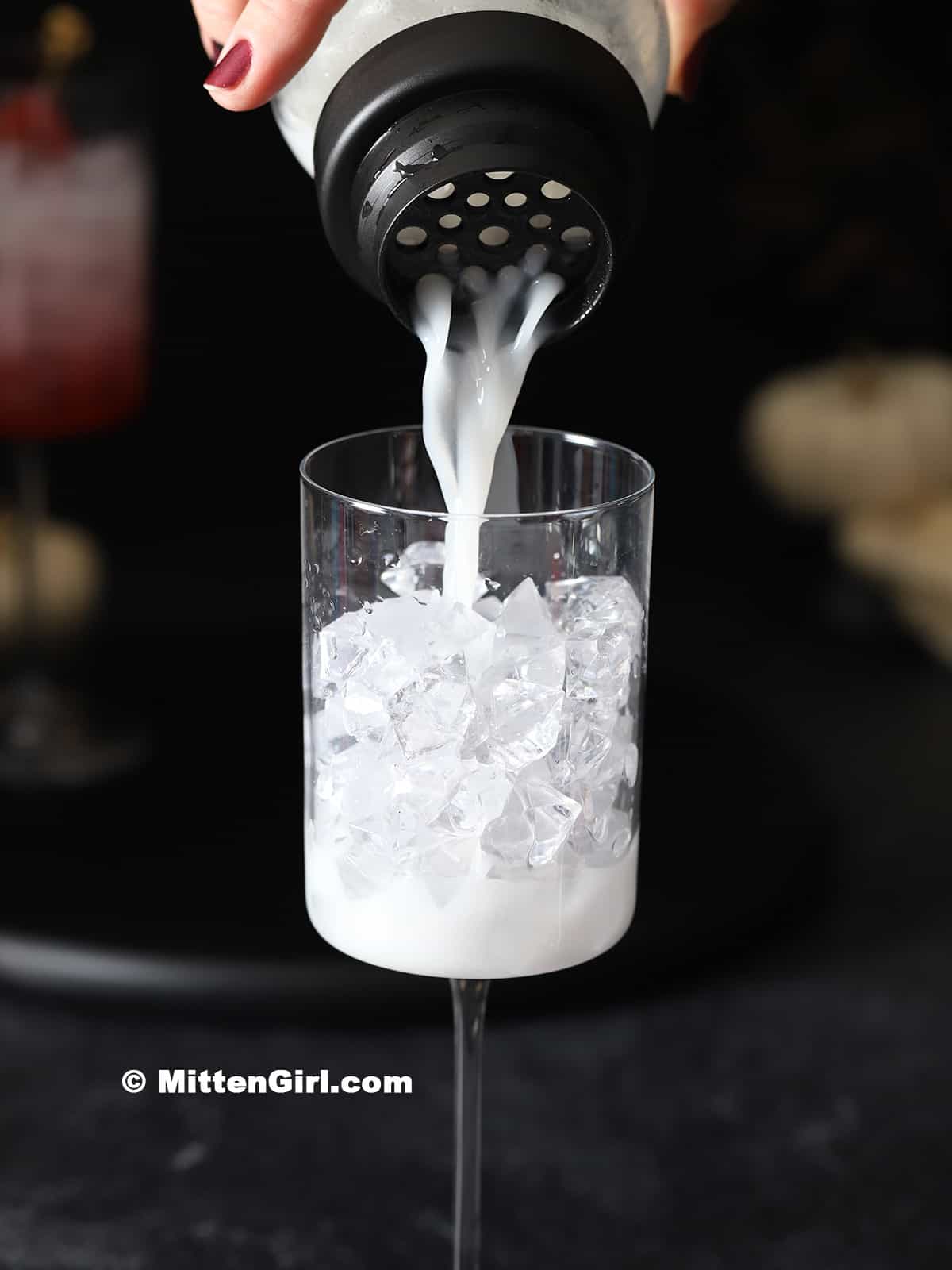 Straining a cocktail into a glass filled with ice.