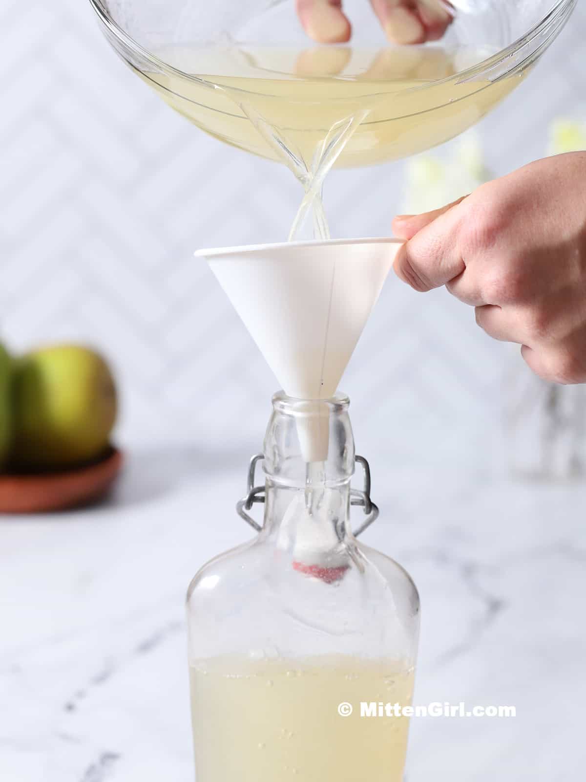 Pear syrup being poured into a glass bottle.