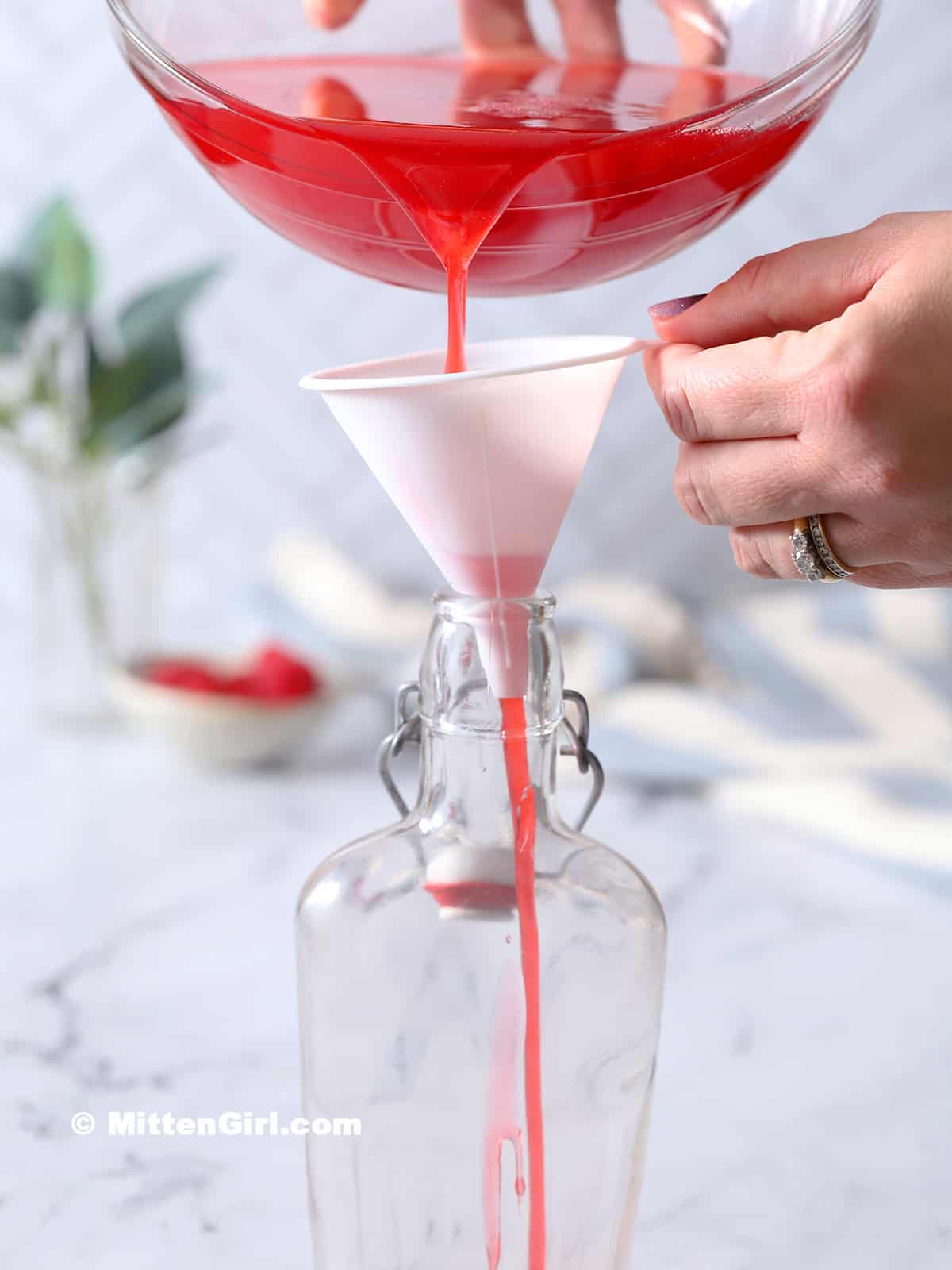 Syrup being poured from a bowl through a funnel and into a glass jar.