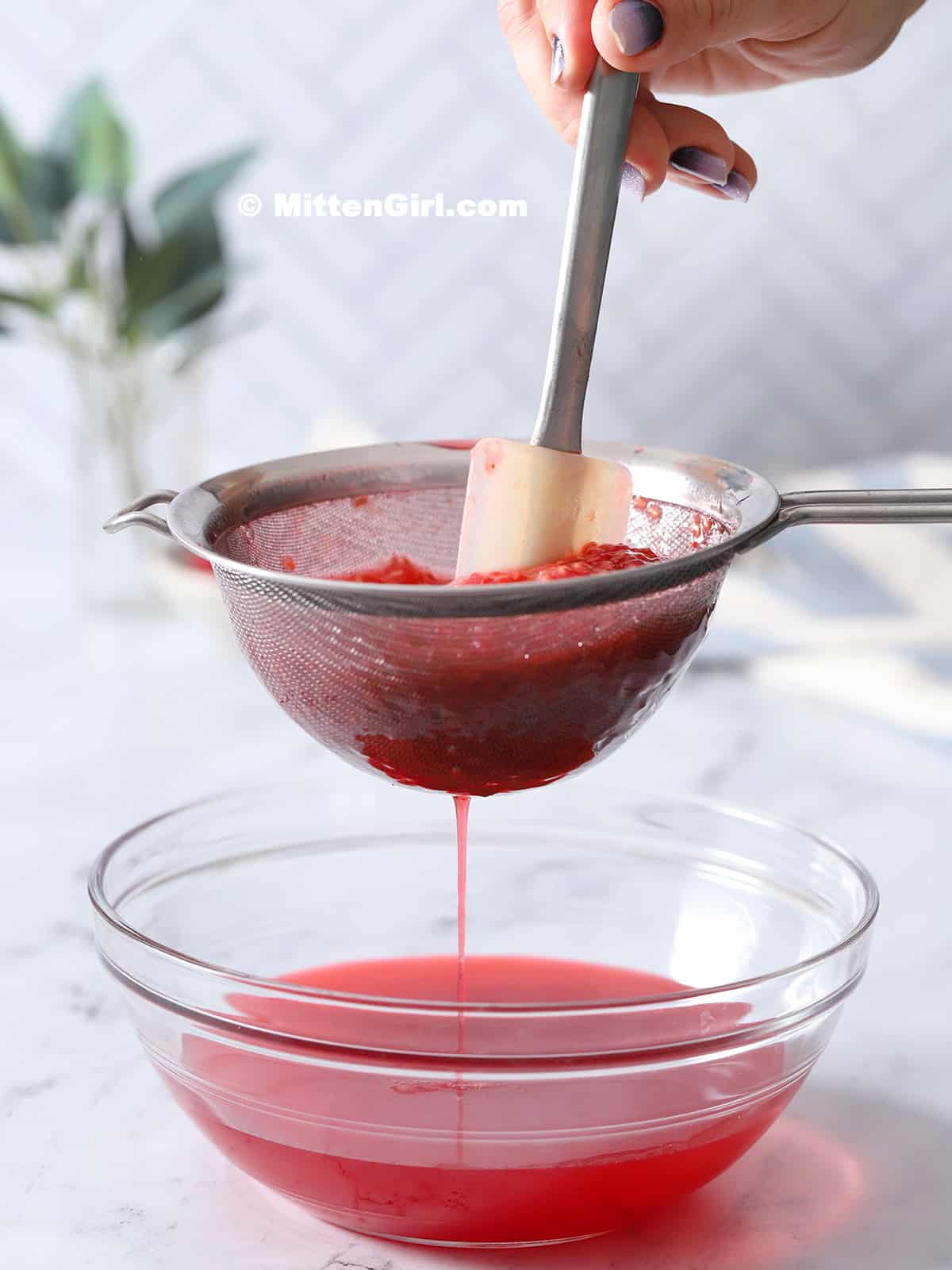 A spatula stirring raspberry syrup through a sieve.