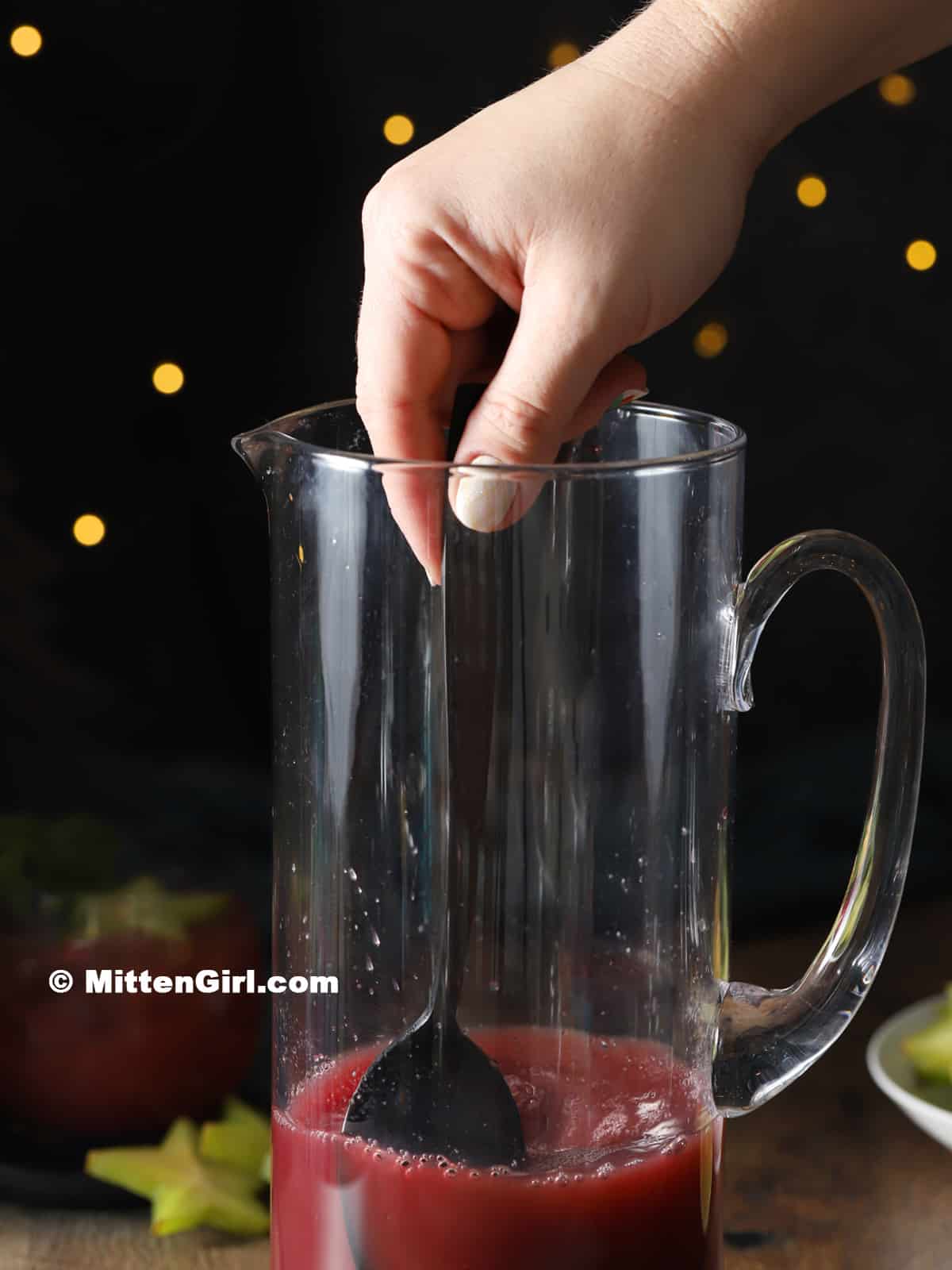 A hand stirring a pitcher of punch.