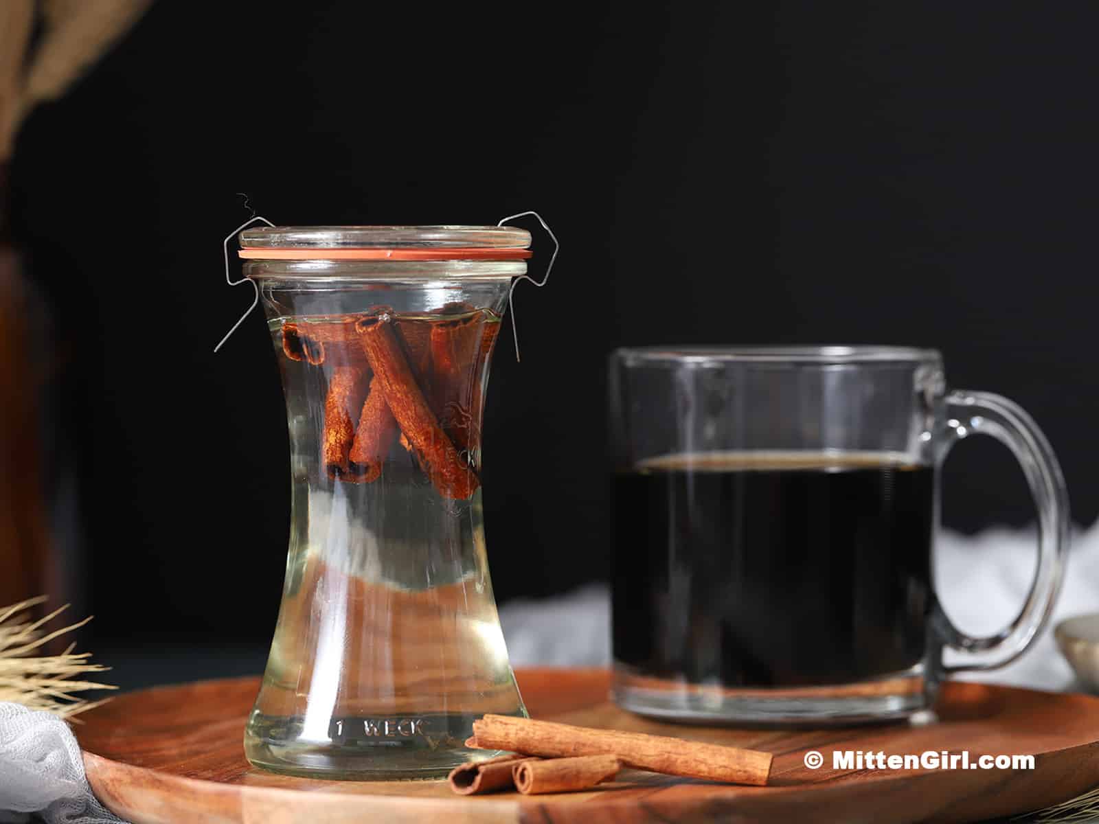 A glass jar of cinnamon simple syrup with a cup of coffee.