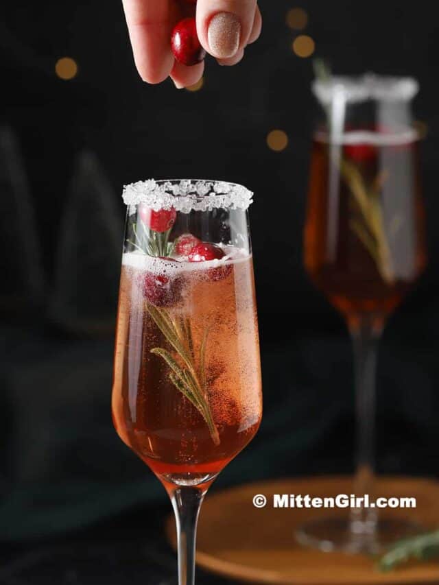 Cranberries being dropped into a glass of cranberry mimosa.