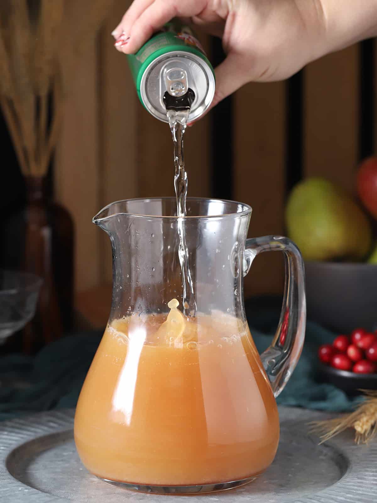 A hand pouring ginger ale into a pitcher of non-alcoholic apple cider punch.
