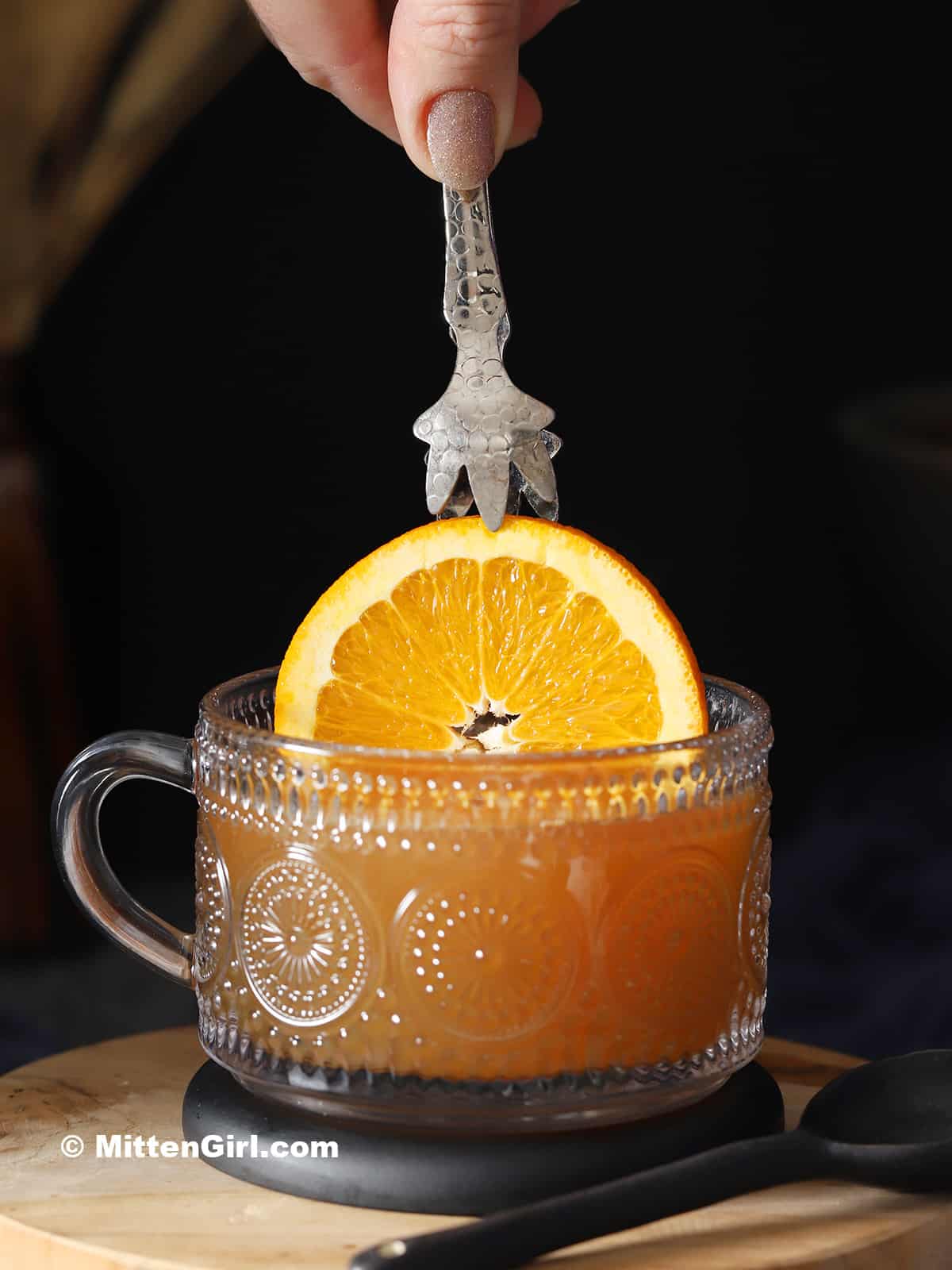 A slice of orange being placed in a mug of hot toddy. 