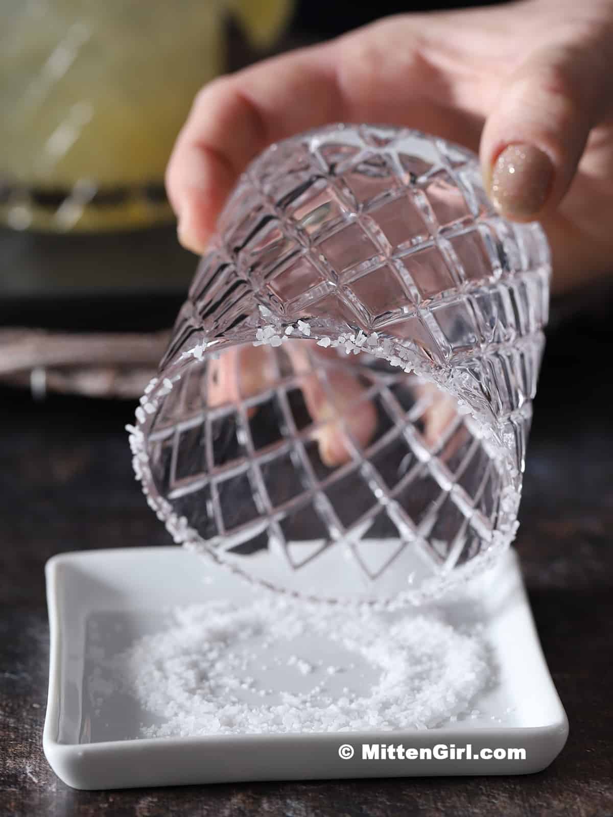 A hand dipping a rocks glass in course salt.