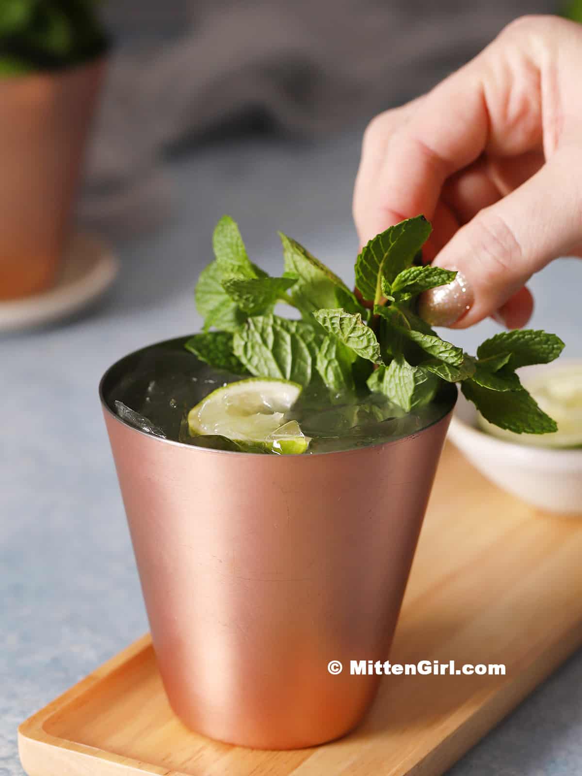 A hand garnishing a moscow mule mocktail with mint.