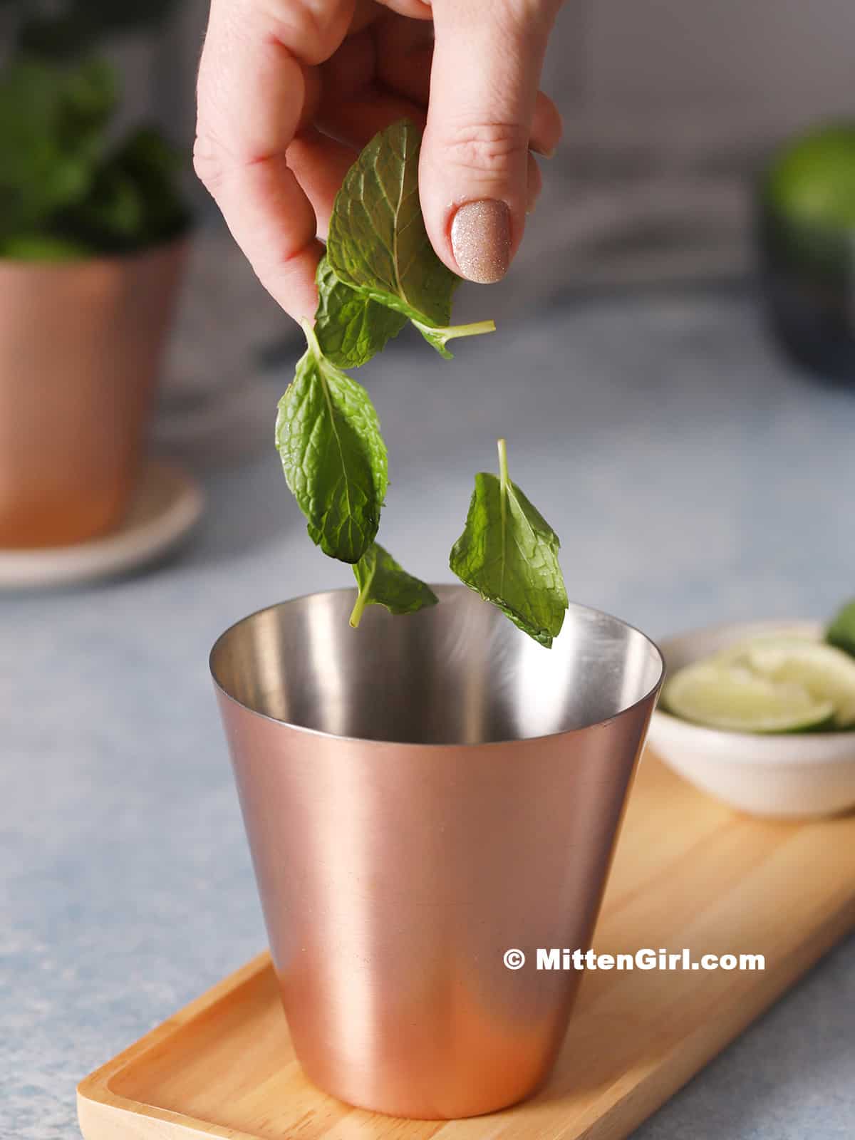Mint leaves being dropped into a copper cup.