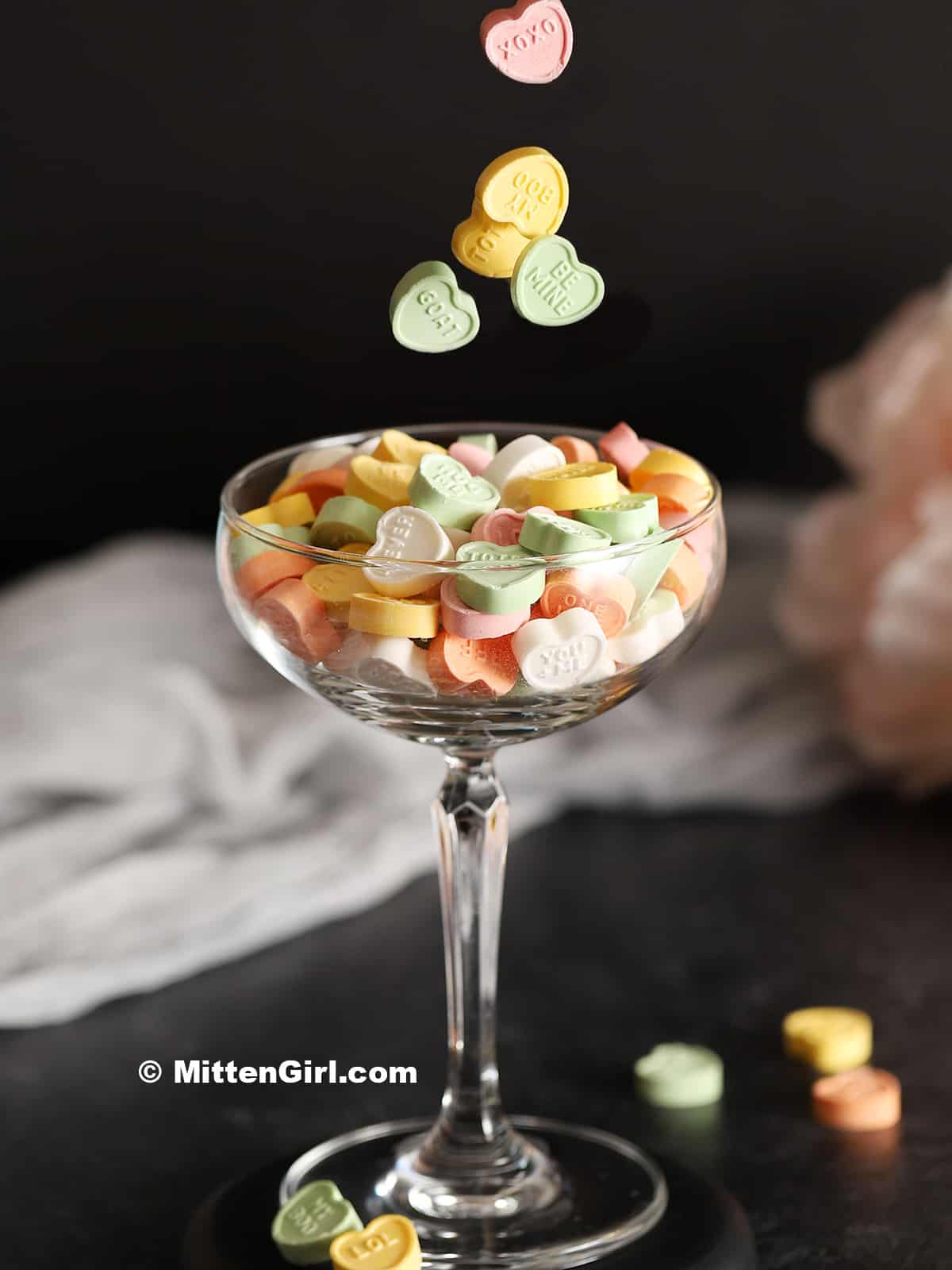 Conversation heart candies falling into a coupe glass.