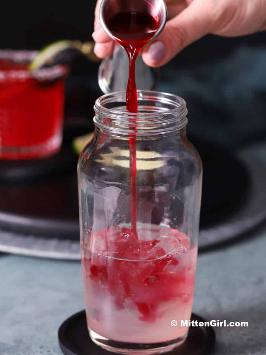 Blackberry syrup being poured into a cocktail shaker.