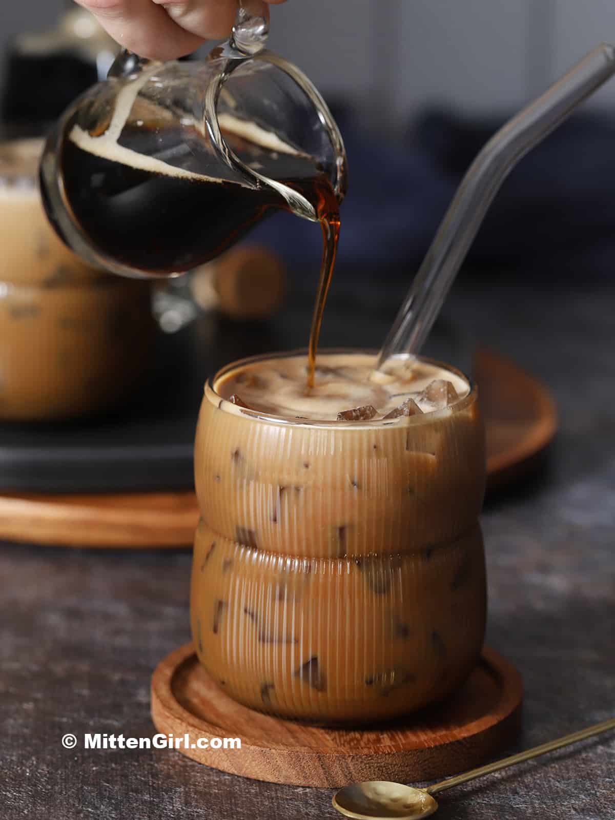 Coffee syrup being poured into a glass of iced coffee.