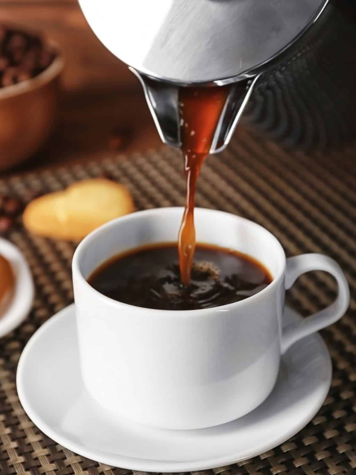 A coffee pot pouring coffee into a mug.