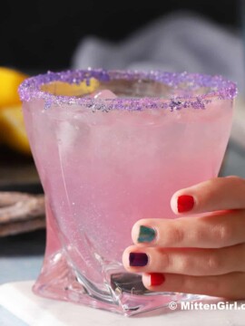A small hand holding on to a glass of unicorn drink lemonade.