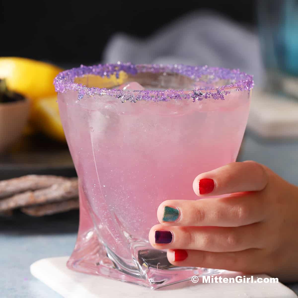 A small hand holding on to a glass of unicorn drink lemonade.