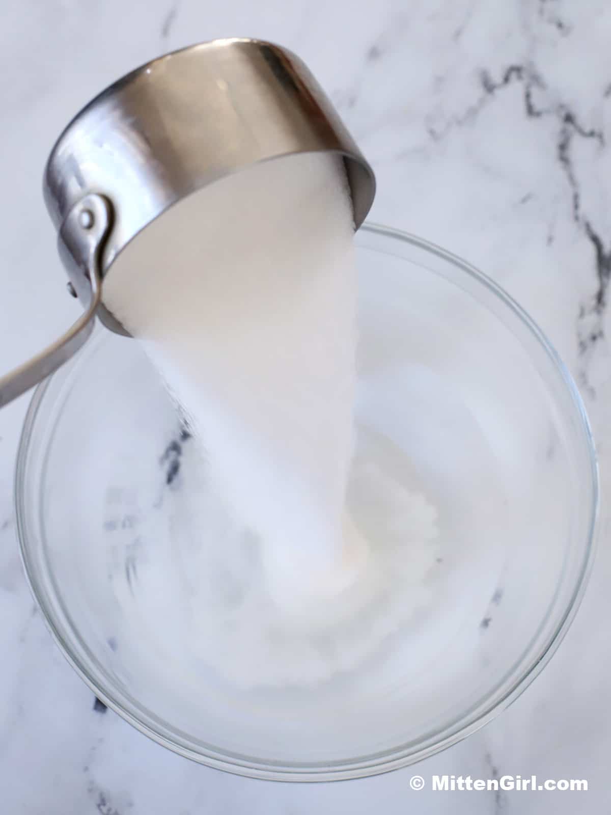 Sugar being poured into a bowl of hot water. 