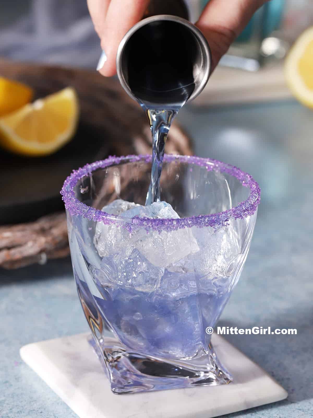 Blue simple syrup being poured into a prepared glass.