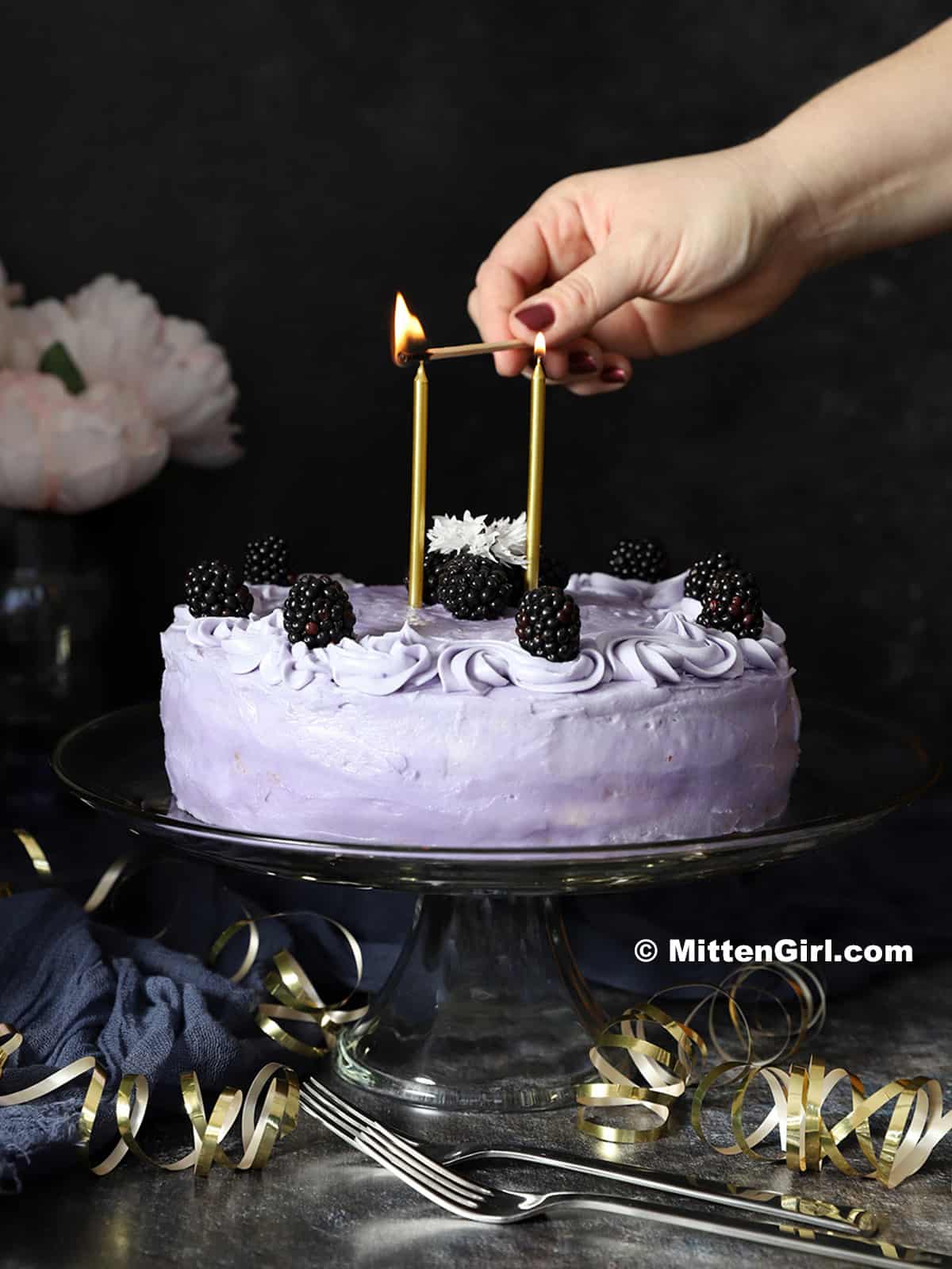 A hand lighting one of two candles on a purple cake.
