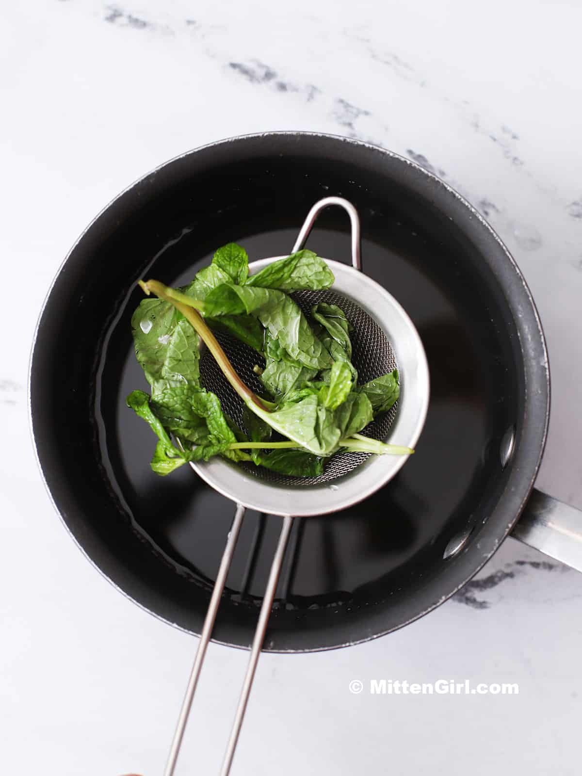 A strainer full of mint leaves over a small pot.