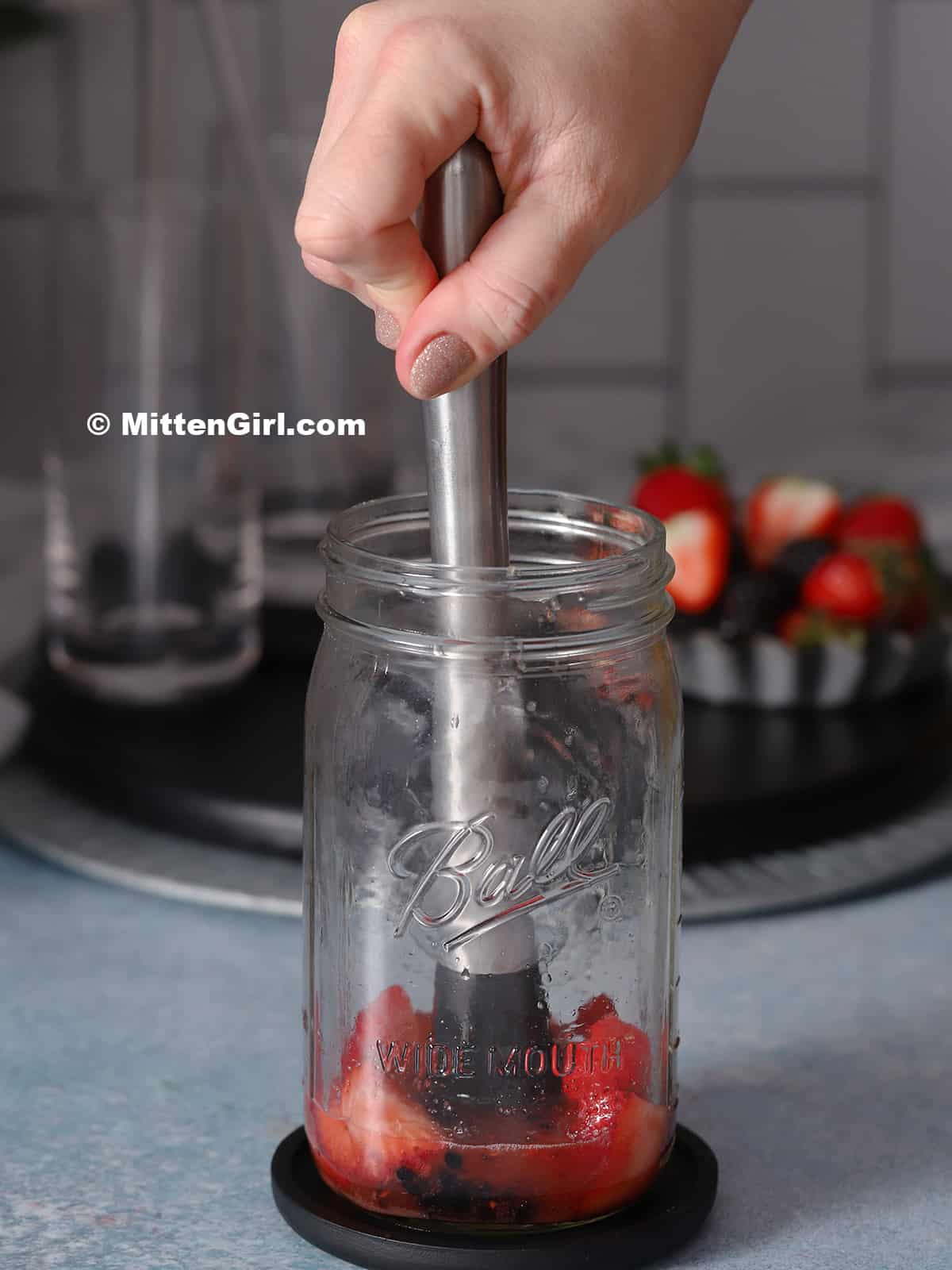 A hand muddling berries in a jar. 