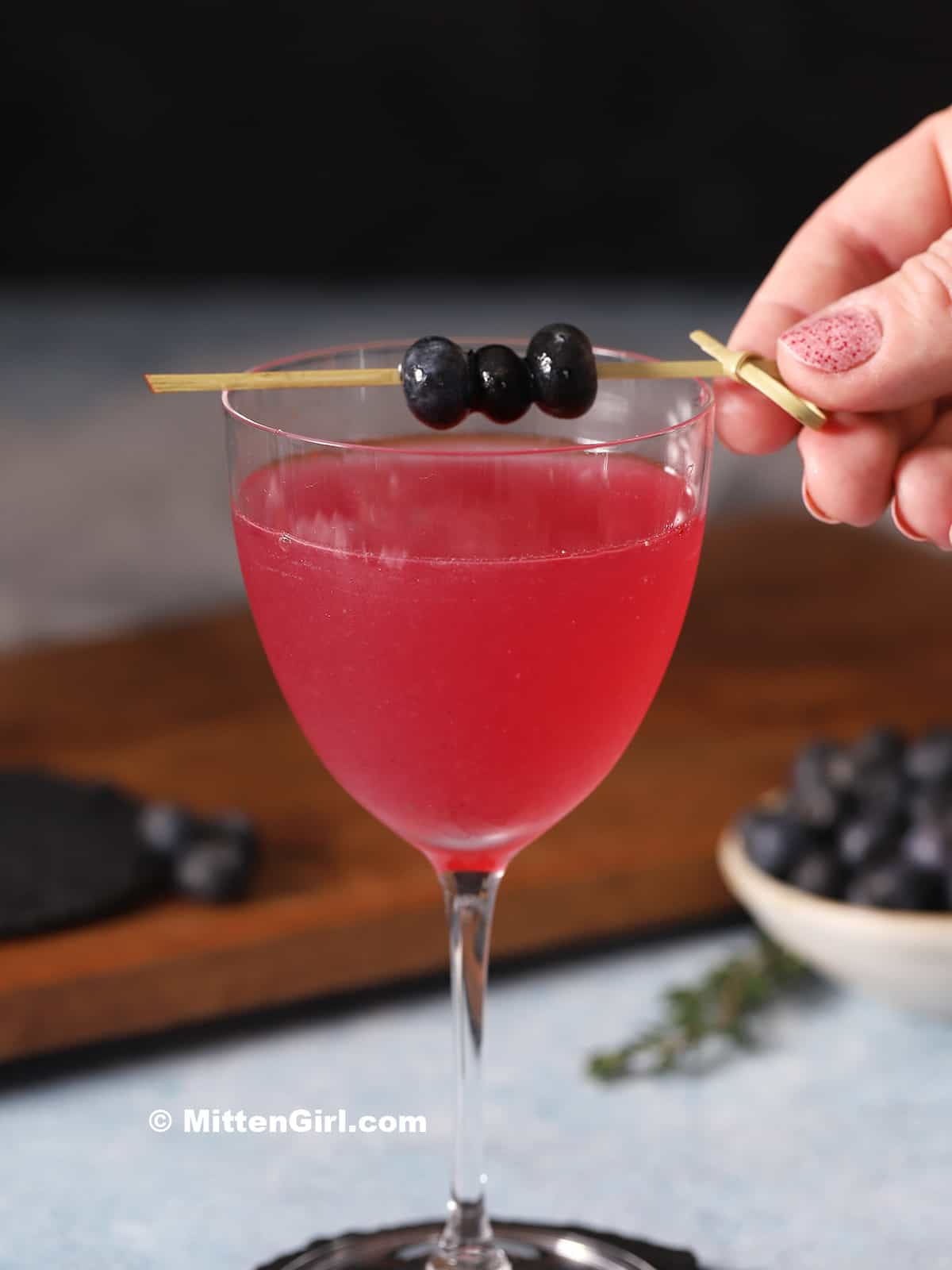 A hand placing blueberrybgarnish on a cocktial.