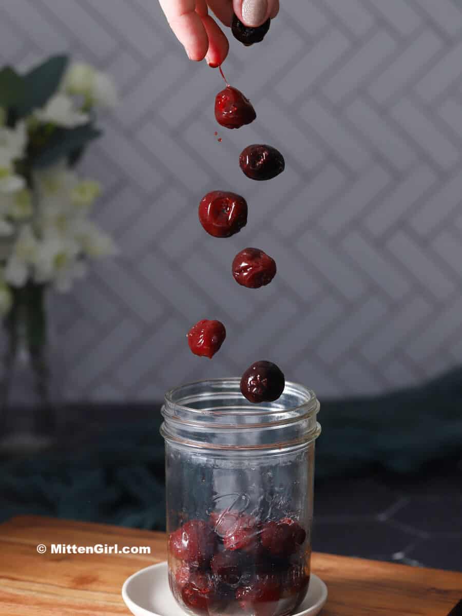 Cherries being dropped into a mason jar.
