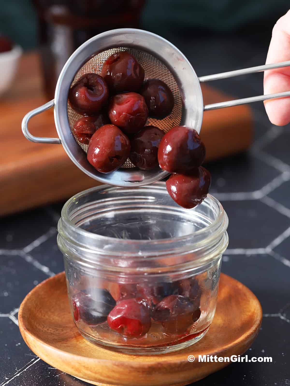 Cherries being poured from a strainer into a small mason jar.