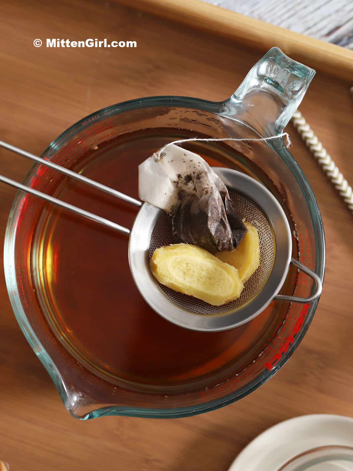 A mesh strainer holding ginger root and a tea bag.
