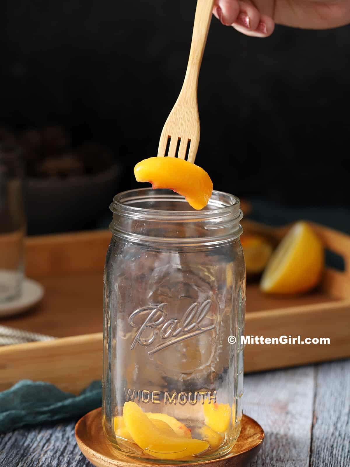 A fork dropping peach slices into a mason jar.