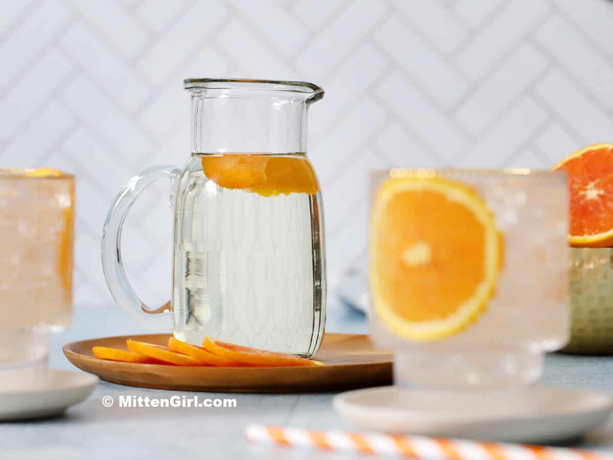 A glass jar of orange syrup with orange peels floating in it.