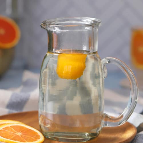A glass pitcher of orange simple syrup.
