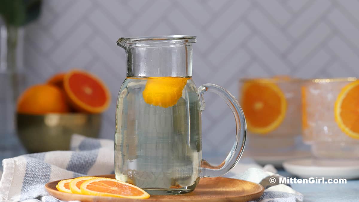A glass pitcher of orange simple syrup. 