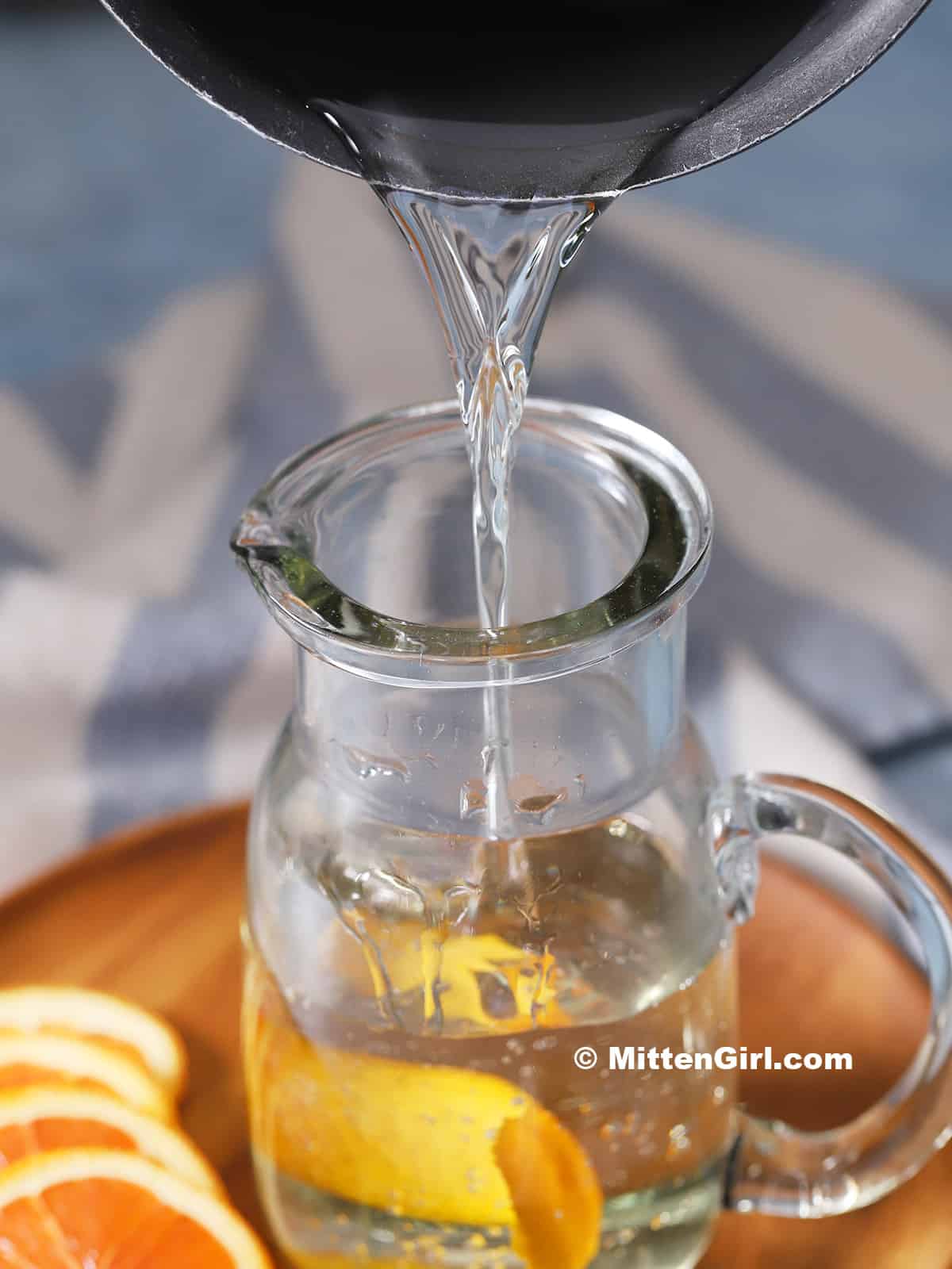 Orange simple syrup being poured into a glass container.