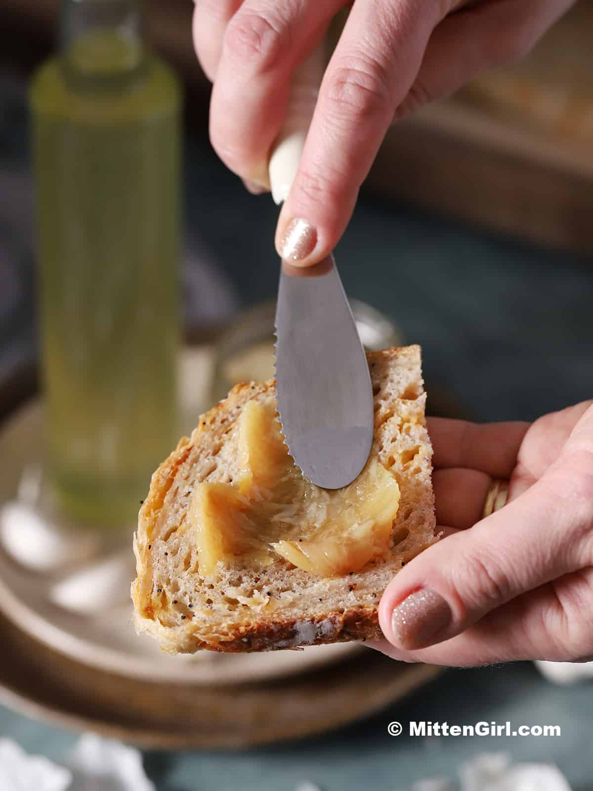 A hand spreading a clove of garlic confit on a slice of bread.