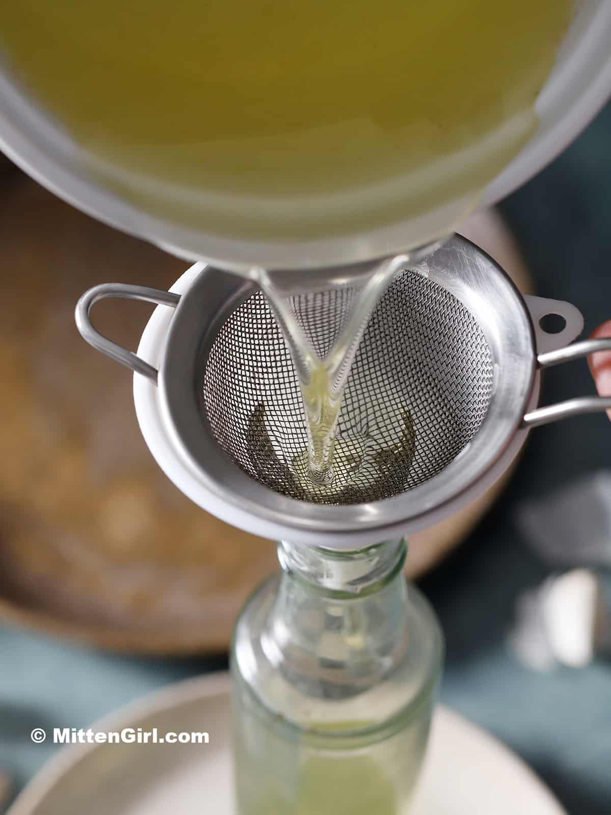The oil from garlic confit being poured through a strainer into a bottle.