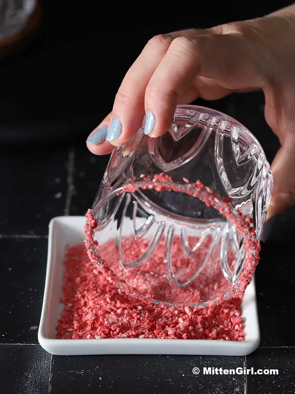 A glass being run through a plate of salt and crushed freeze-dried strawberries.