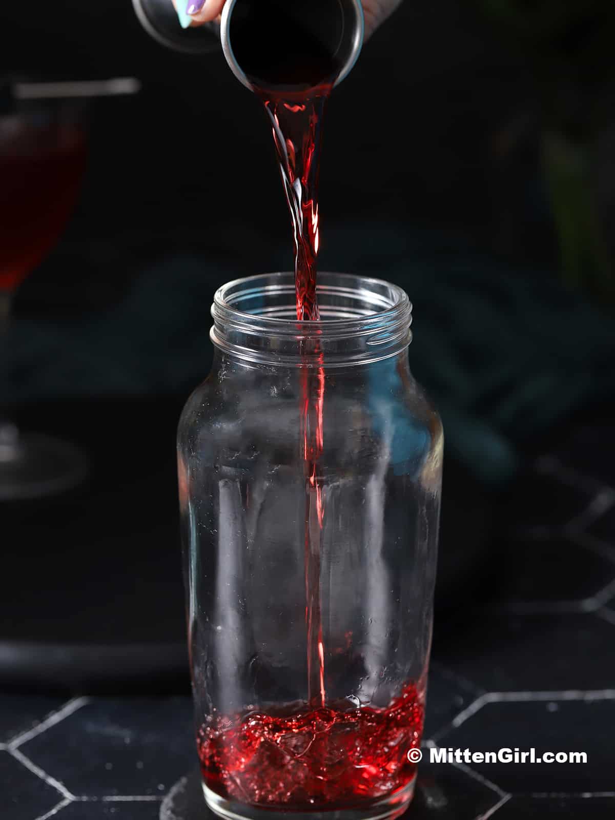 Cherry vodka being poured into a cocktail shaker.