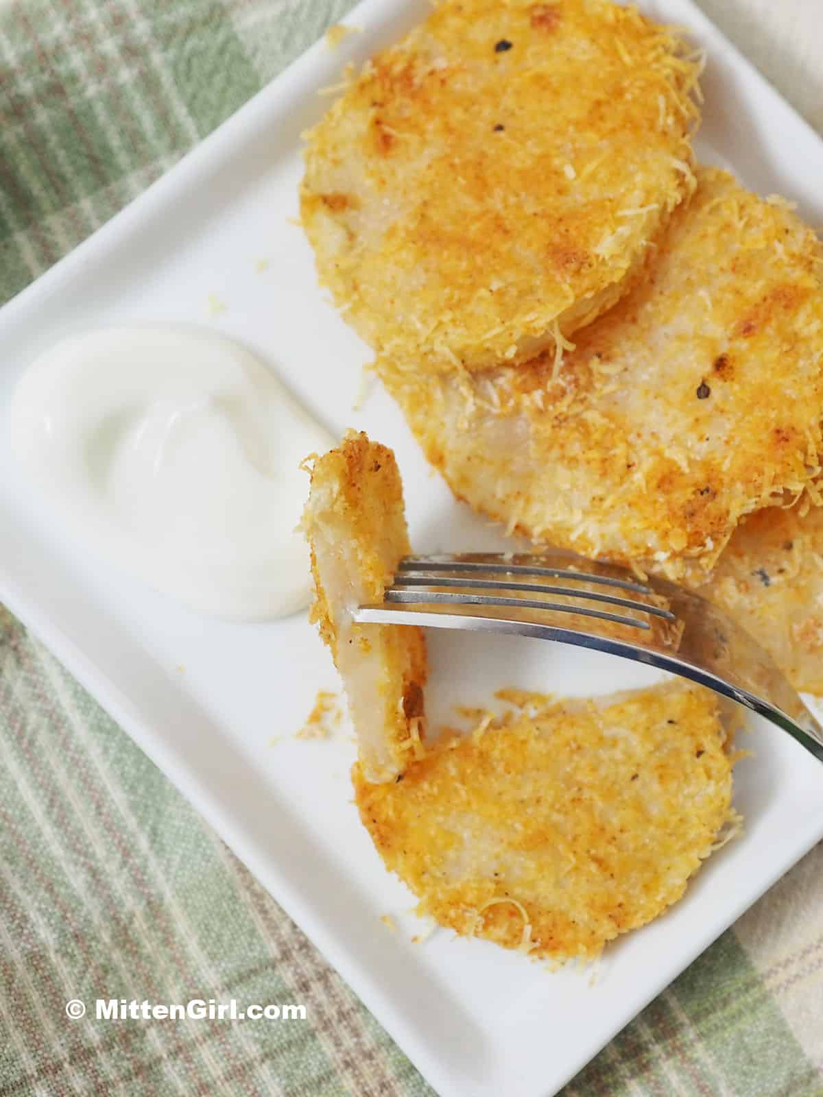 A fork dipping a potato round into sour cream. 