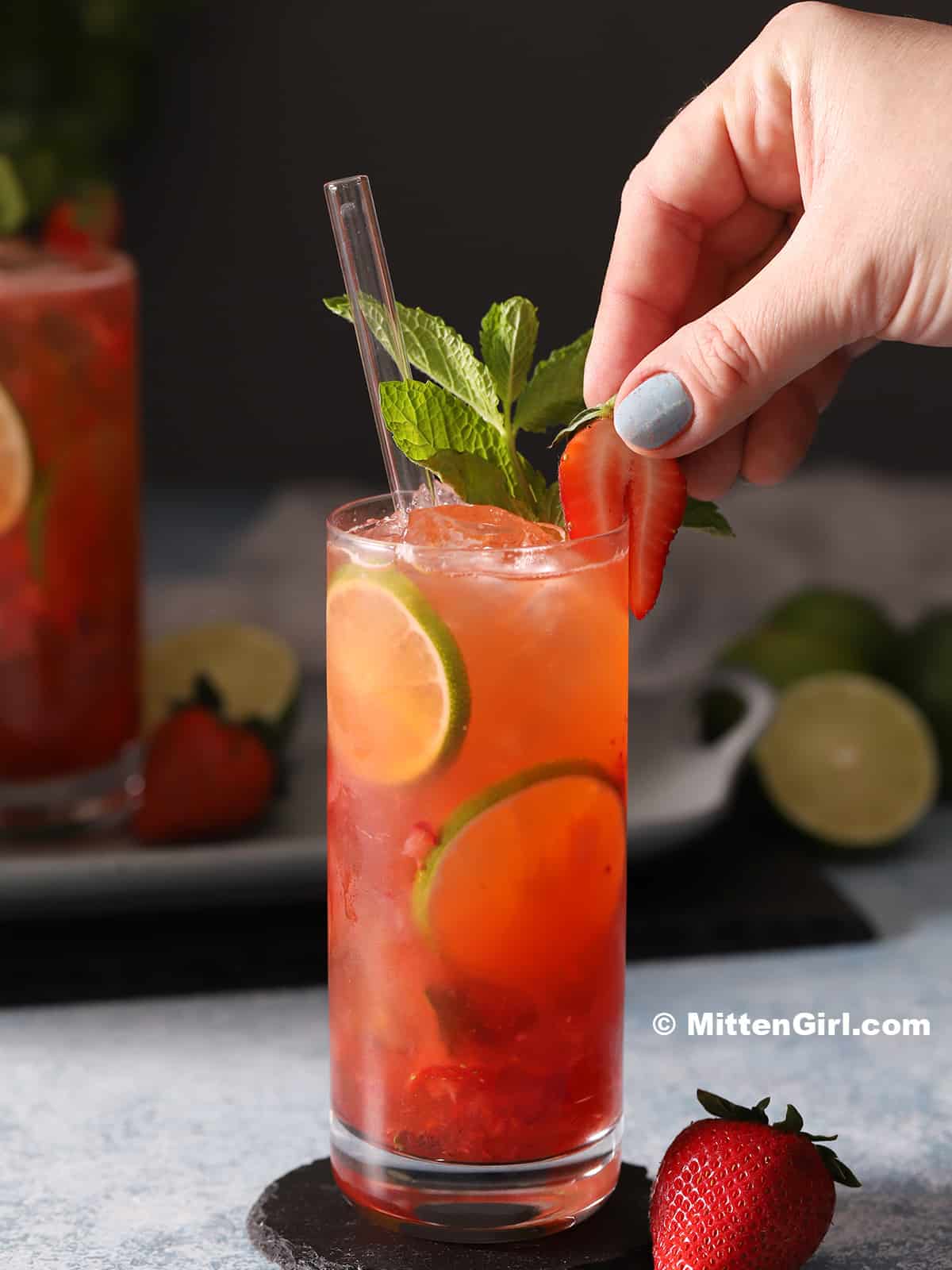 A hand garnishing a mojito mocktail with a strawberry.