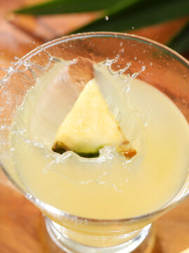 A pineapple wedge splashing down into a martini glass full of cocktail.