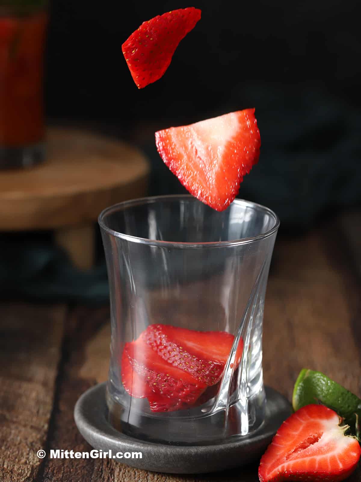 Strawberry slices being dropped into a rocks glass.