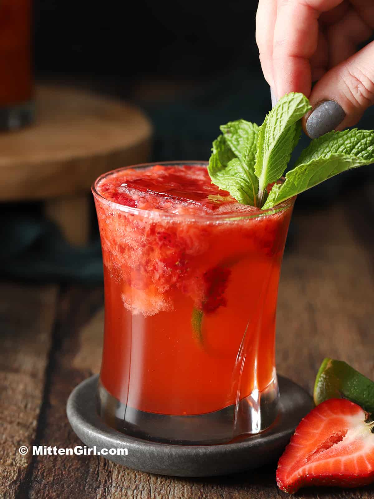 A hand garnishing a strawberry gin cocktail with a mint sprig.