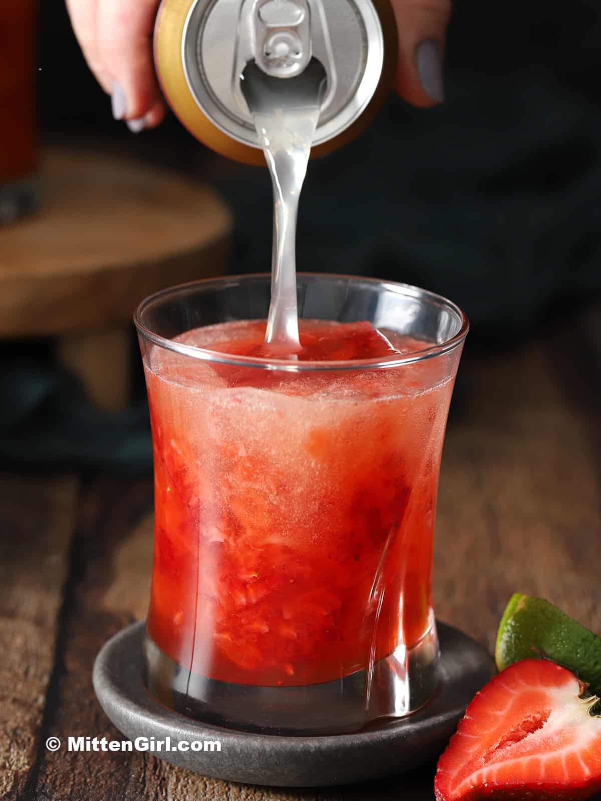 Ginger beer being poured into a rocks glass filled with strawberry cocktail.