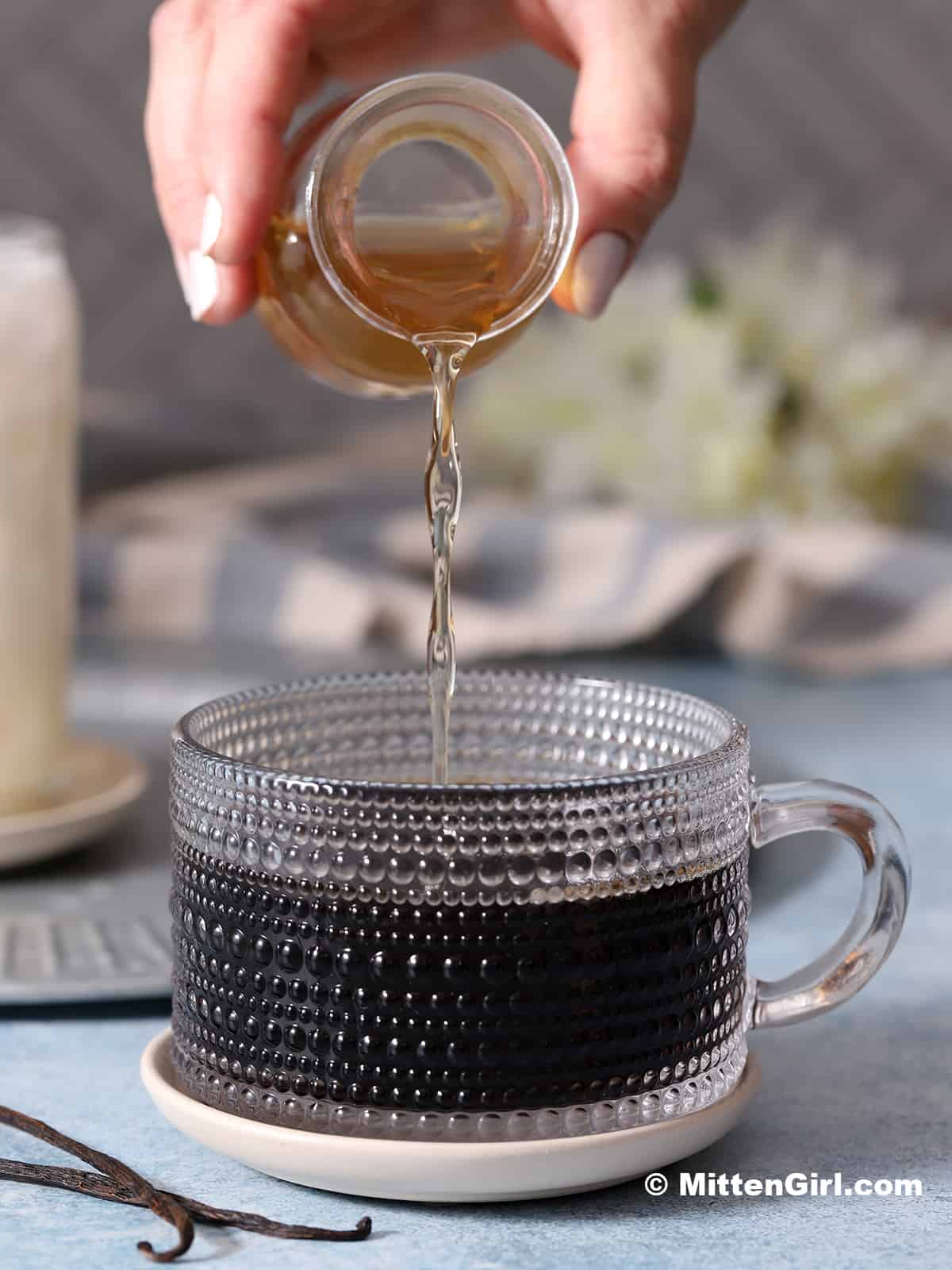 Vanilla syrup being poured into a cup of coffee.